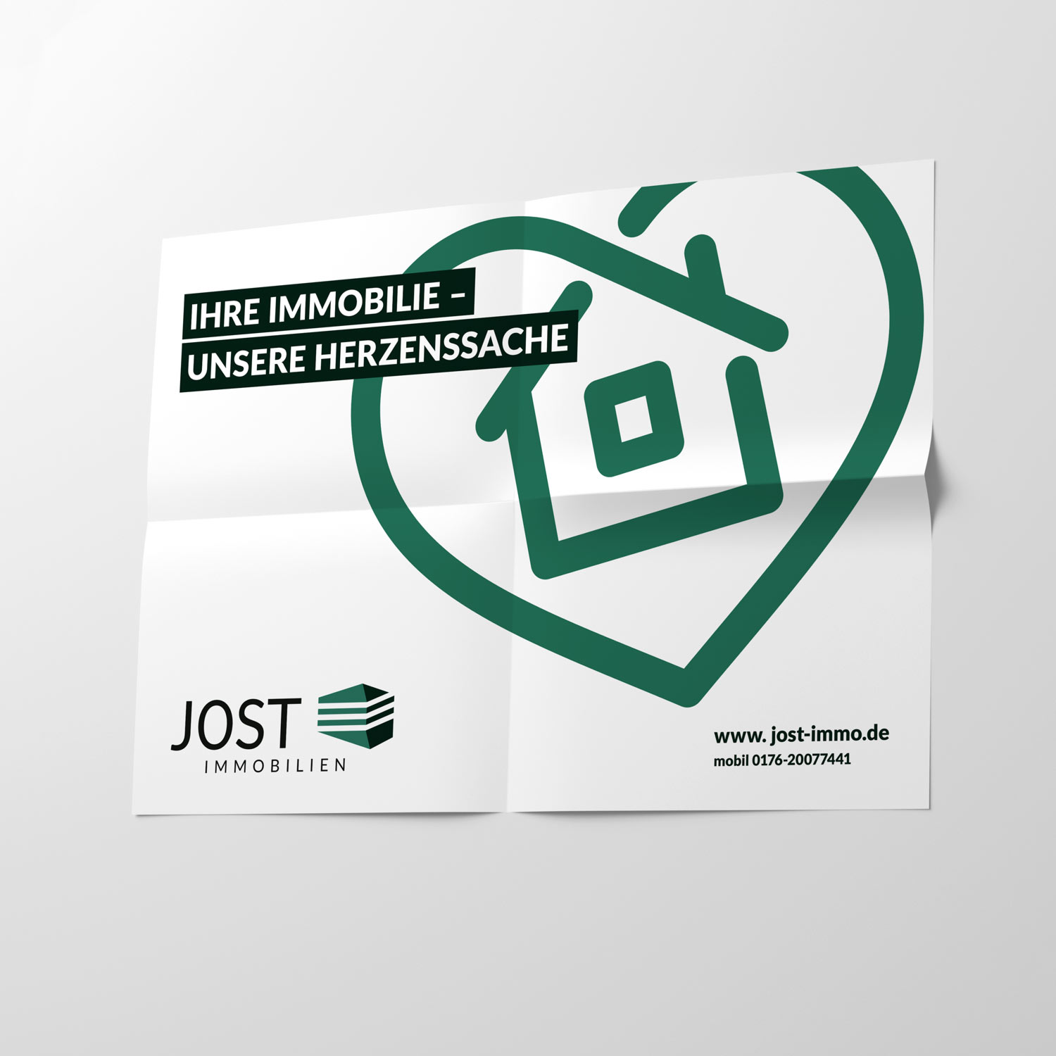 Plakat von Jost mit Aufschrift "Ihre Immobilie - unserer Herzenssache" und grünem Herz mit Haus-Illustration und Jost Logo